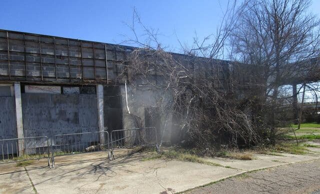 Boarded-up front of the vacant commercial building, with brush piled along the fence, before demolition