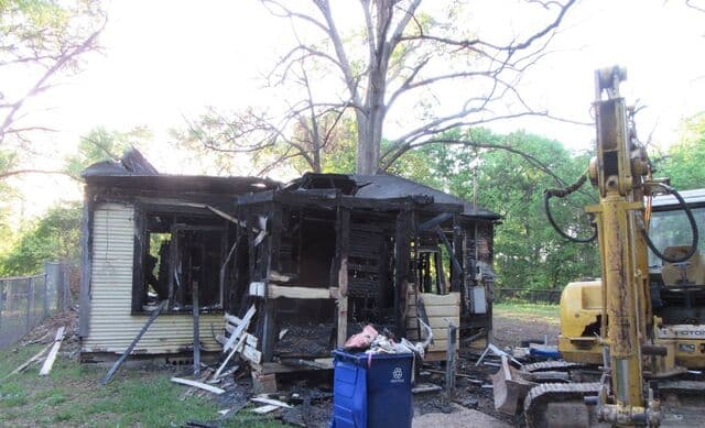 Fire-damaged house in Shreveport with an excavator beside it, ready for demolition