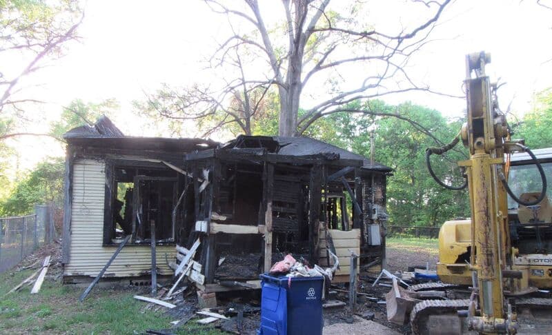 Fire-damaged house in Shreveport with an excavator beside it, ready for demolition