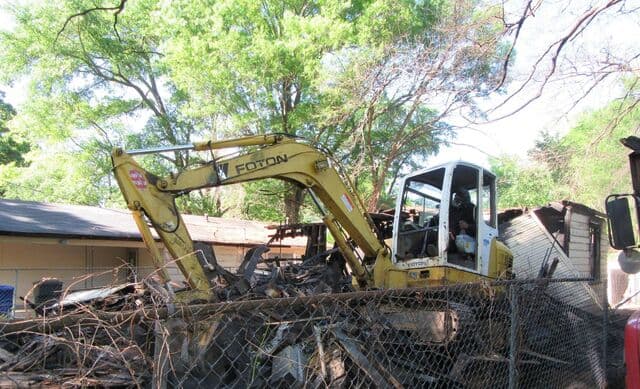 Yellow mini excavator tearing down a fire-damaged house