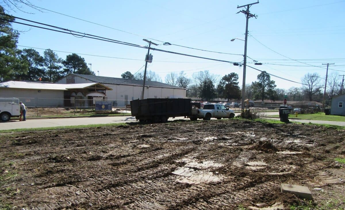 Graded residential lot after demolition, with a loaded debris trailer at the curb