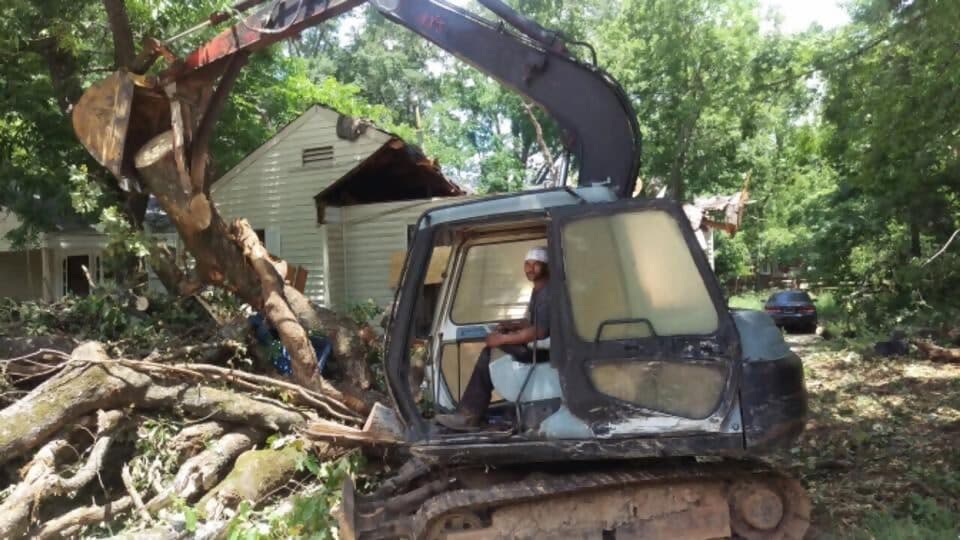 Excavator operator lifting a fallen tree away from a house