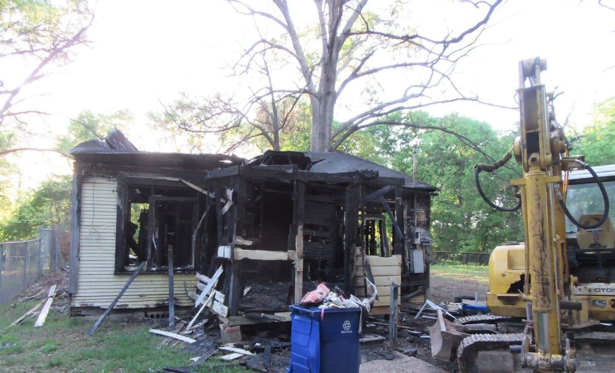 Fire-damaged house in Shreveport with an excavator beside it, ready for demolition