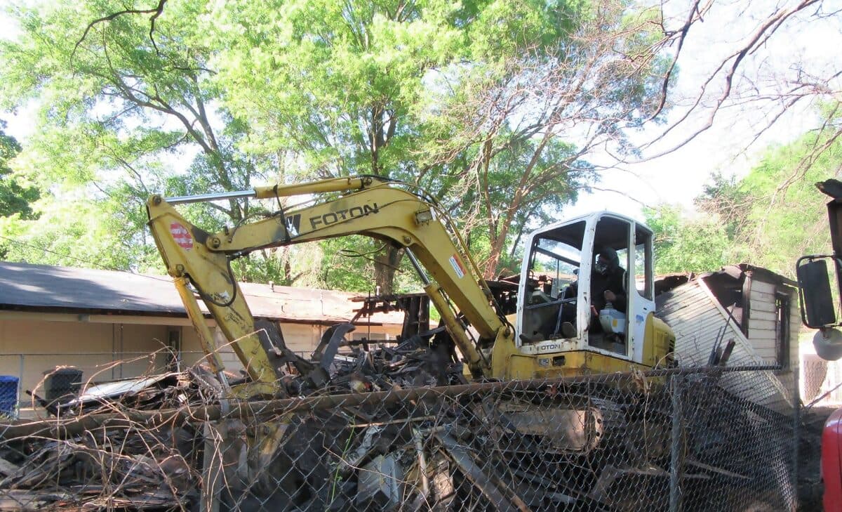Yellow mini excavator tearing down a fire-damaged house